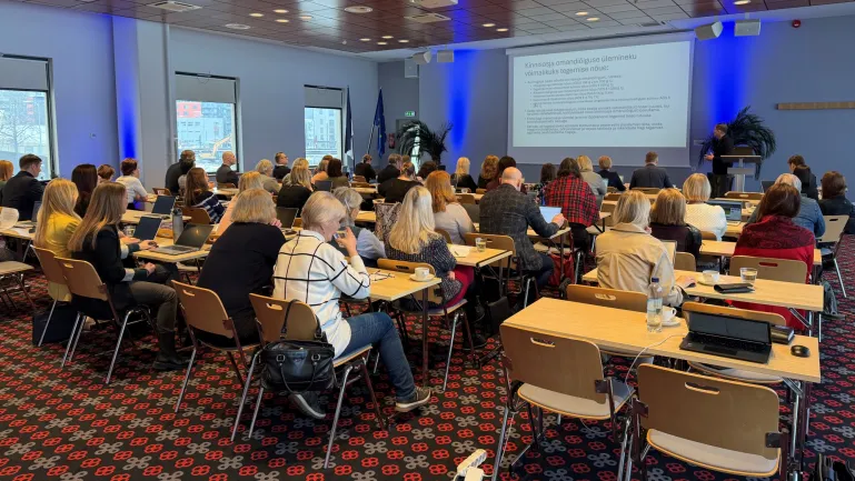 Koolitusel osalejad istuvad laudade taga ning loevad seinale kuvatud teavet ja kuulavad koolitajat. 